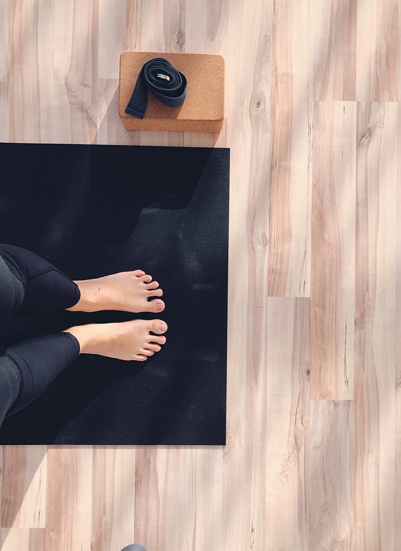 Pies sobre una colchoneta y al lado un bloque y un cinturón de yoga