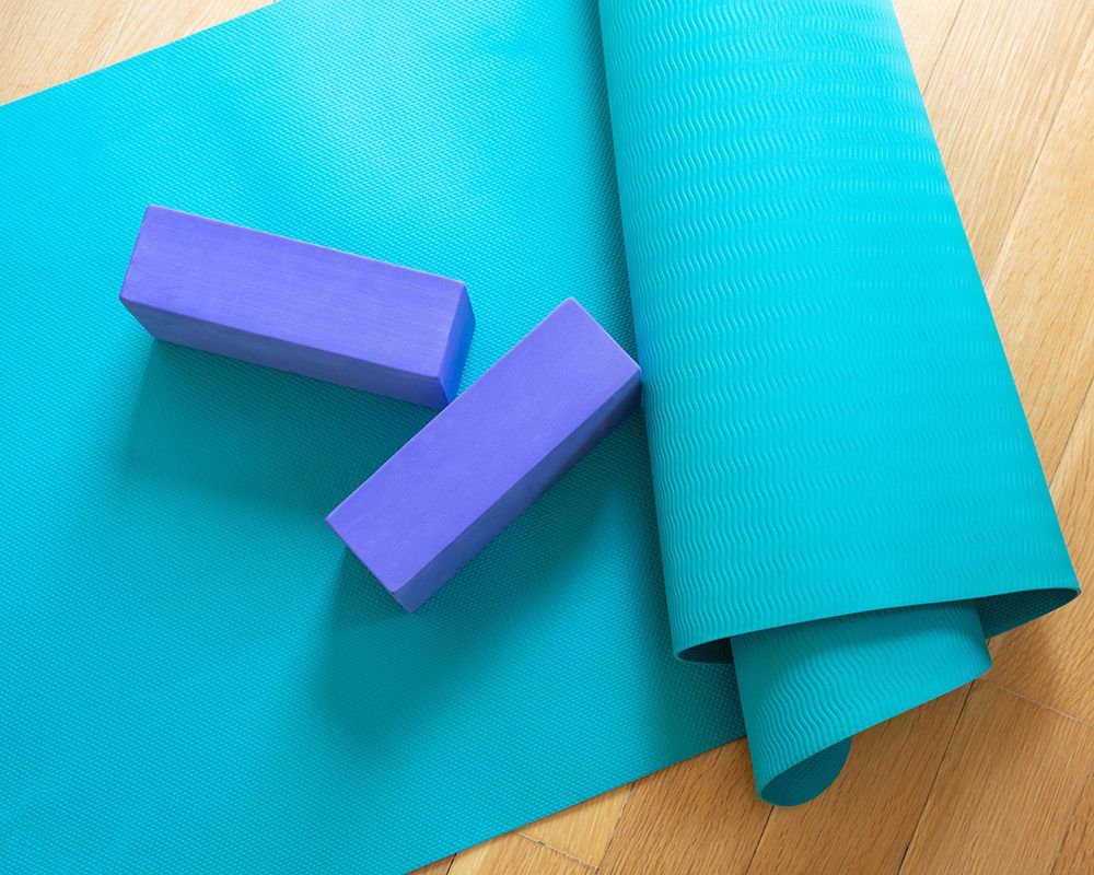 Colchoneta de yoga y ladrillos de ejercicio sobre suelo de madera. Pilates, clase de yoga, entrenamiento en casa y concepto de estilo de vida saludable