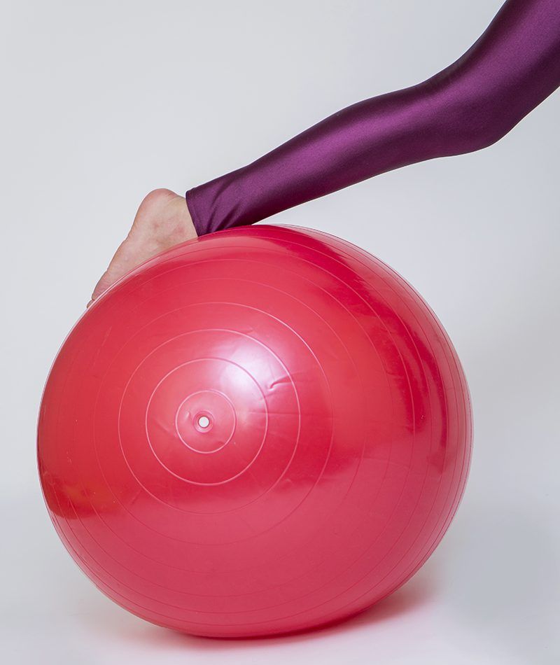 Pierna de mujer encima de pelota de pilates roja